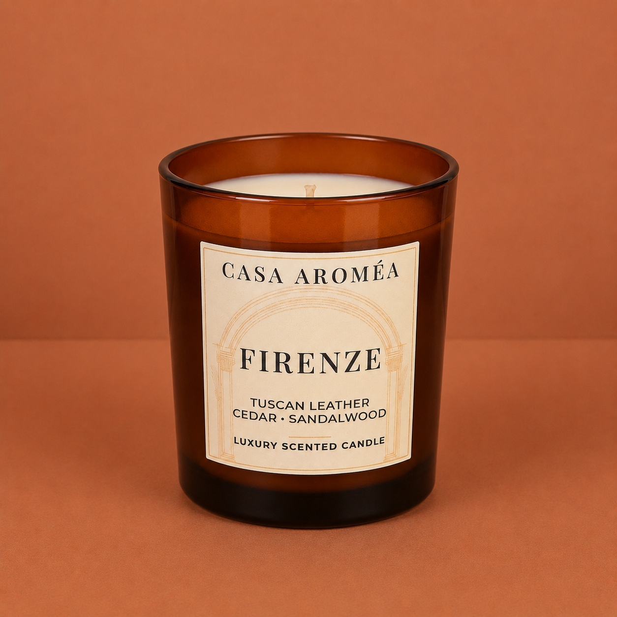 Large Firenze scented candle by Casa Aroméa in an amber glass vessel against a warm terracotta and cocoa-toned textured background