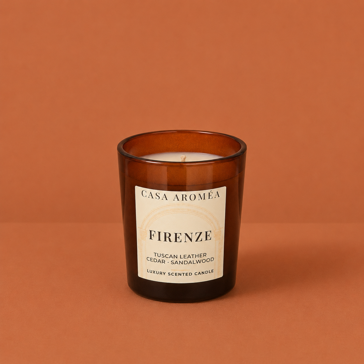 Small Firenze scented candle by Casa Aroméa in an amber glass vessel against a warm terracotta and cocoa-toned textured background