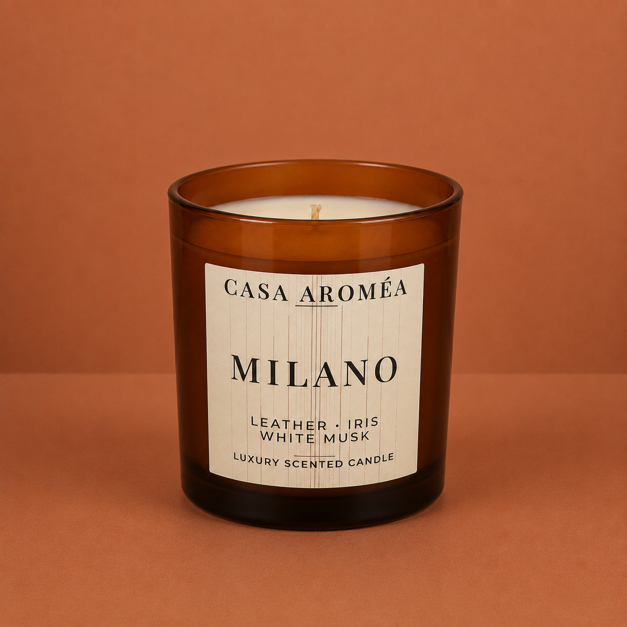 Large Milano scented candle by Casa Aroméa in an amber glass vessel against a warm terracotta and cocoa-toned textured background