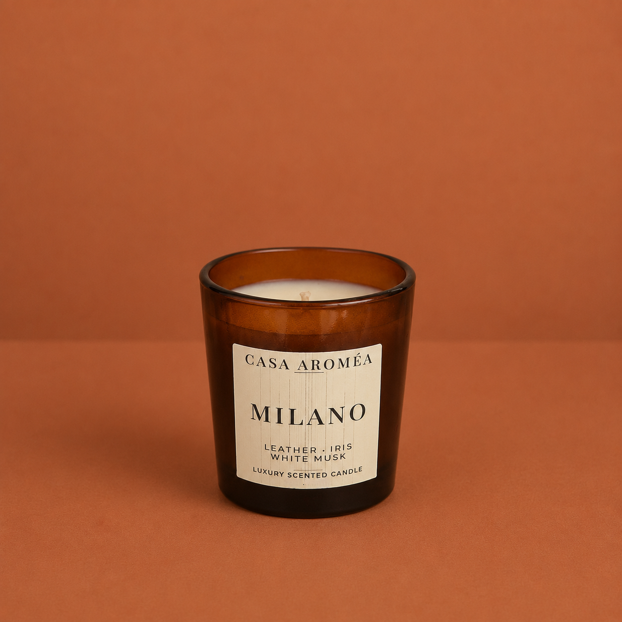 Small Milano scented candle by Casa Aroméa in an amber glass vessel against a warm terracotta and cocoa-toned textured background