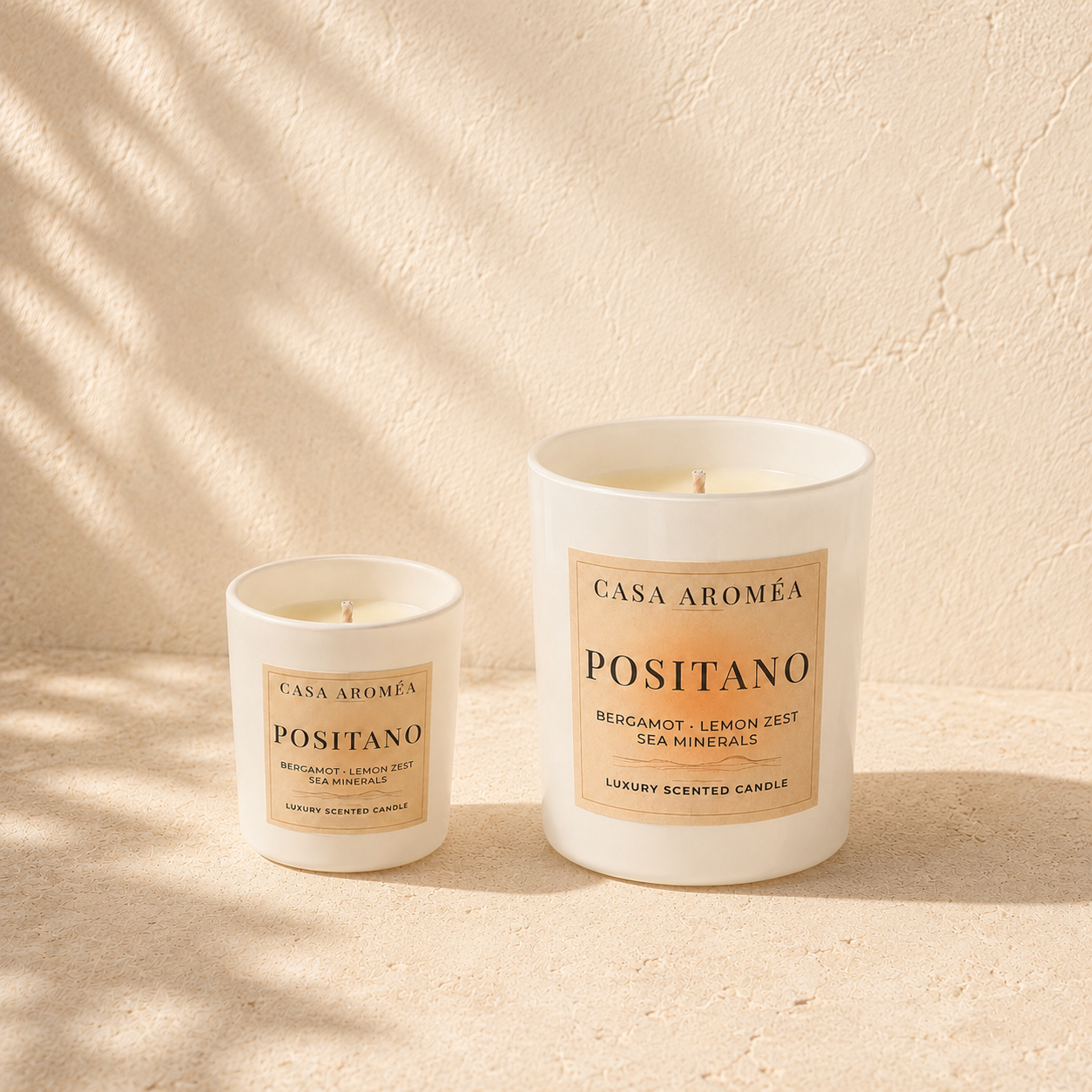 Positano Small and Large scented candles by Casa Aroméa in white glass vessels against a warm Mediterranean-inspired textured background